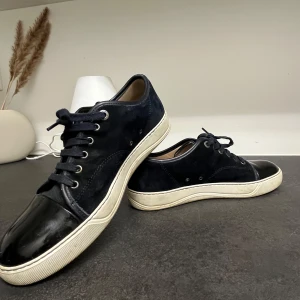 Blå sneakers från Lanvin - Snygga blå sneakers från Lanvin i mocka med skinn på tån. Skorna har en vit sula och klassisk snörning. Perfekta för en stilren look.