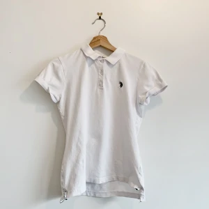 Vit pikétröja från Marcopolo - Snygg vit pikétröja med korta ärmar och klassisk krage. Tröjan har en broderad logga på bröstet och knappar framtill. Perfekt för en stilren och avslappnad look.