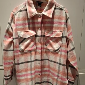 Rutig overshirt från Lindex - Säljer en snygg rutig overshirt från Lindex i rosa, vit och svart. Jackan har långa ärmar och knappar framtill. Perfekt för lager-på-lager-stil och har två praktiska bröstfickor med lock.