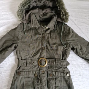 Grön parkajacka från Eminent - Säljer denna fantastiska jacka från Eminent 🌿 I fint skick! Khakifärgad modell med pälsluva och unikt skärp. Även två fickor framtill. Stängs med knappar. Både pälsen och hela luvan kan tas av, alltså tre jackor i en!  Pris är självklart förhandlingsbart 😊 Hör gärna av er vid frågor och glöm inte att kolla in garderoben för fler liknande plagg! 💕