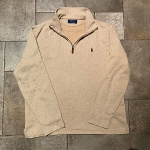 Ralph Lauren Quarter Zip Medium - Säljer en stilren beige Half/Quarter Zip från Polo Ralph Lauren med dragkedja och broderad logga på bröstet. Tröjan har långa ärmar och är tillverkad i ett mjukt material som passar perfekt för kyligare dagar. Extremt gott skick! 