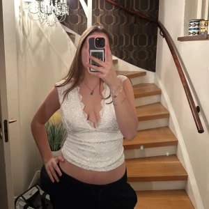 Vit spetslinne från Shein - Säljer en vit spetslinne från Shein med v-ringning och öppen rygg. Toppen har ett fint spetsmönster och är ärmlös, perfekt för sommarens varma dagar. Den är tillverkad i polyester och elastan för en bekväm passform.