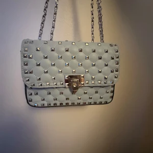 Ljusblå quiltad axelväska med nitar - Snygg ljusblå axelväska med quiltad design och silverfärgade nitar. Väskan har en kedjerem och ett stilrent lås framtill. Perfekt för att ge din outfit en edgy touch.