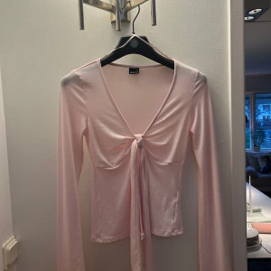 Rosa långärmad topp från Gina Tricot!! - Säljer en söt rosa långärmad topp från Gina Tricot. Toppen har en v-ringad design med knyt framtill, vilket ger en fin detalj. Säljer då den inte kommer till användning!