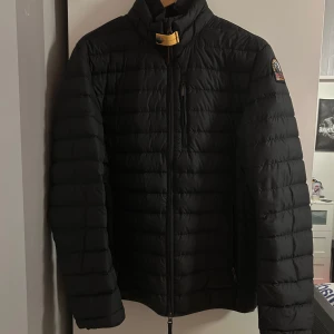 Svart pufferjacka från Parajumpers - Säljer en svart pufferjacka från Parajumpers med broderad logga på ärmen. Jackan har en dragkedja framtill och är quiltad för extra värme. Perfekt för kyliga dagar med sin stilrena design och praktiska fickor. Använd väldigt sparsamt, pris kan diskureras