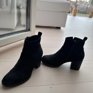 Svarta mocka boots med klack - Snygga svarta boots i mocka med en stabil klack. Perfekta för både vardag och festliga tillfällen. De har en dragkedja på sidan för enkel på- och avtagning.