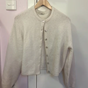 Vit kofta från Gina Tricot - Säljer en stilren vit/crem kofta från Gina Tricot i premiumkvalitet. Koftan har långa ärmar och knappar framtill, perfekt för en mysig look. Passar bra till både vardag och speciella tillfällen.