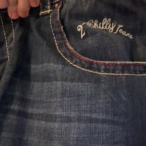 Vintage Mörkblå jeans från Chilly Jeans - Snygga mörkblå jeans från Chilly Jeans med kontrastsömmar i rött och vitt. Klassisk femficksdesign med broderad logga på bakfickan. Perfekta för en avslappnad stil.