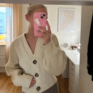 Beige stickad kofta med knappar - Säljer en mysig beige stickad kofta med stora knappar framtill. Koftan har en v-ringad design och långa ärmar, perfekt för kyligare dagar. Passar bra till både jeans och kjol.