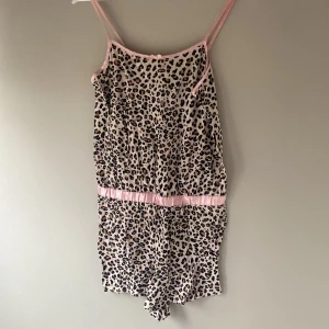 Leopardmönstrad pyjamasdress - Säljer en leopardmönstrad ärmlös pyjamasdress med rosa detaljer. Pyjamasen har smala axelband och en elastisk midja för en bekväm passform. Perfekt för en djärv och trendig look.