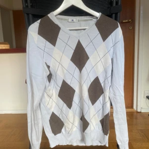 Ljusblå tröja med argylemönster från JP - Snygg ljusblå tröja med klassiskt argylemönster i brunt och beige från JP. Tröjan har långa ärmar och en rund halsringning. Snygg och bekväm.
