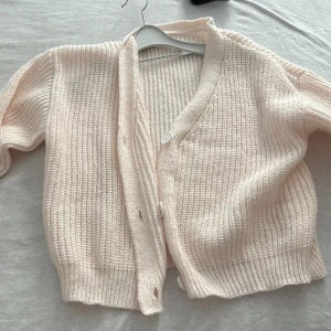 Beige stickad kofta - Mysig beige stickad kofta med knappar framtill. Perfekt för kyliga dagar med sin ribbade struktur och bekväma passform. Ett måste i garderoben för en stilren look.