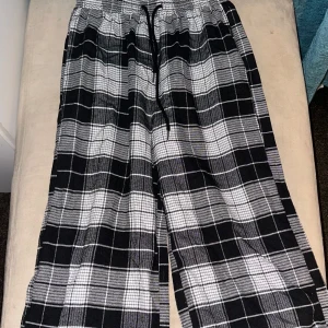 Svartvitrutiga byxor med snörning - Snygga och bekväma byxor i svart och vitt rutmönster. De har en elastisk midja med snörning för justerbar passform. Perfekta för en avslappnad stil.