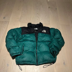 Grön och svart dunjacka från The North Face - Säljer en grön och svart dunjacka från The North Face. Jackan har en dragkedja framtill och är långärmad. Perfekt för kyligare väder med sin pufferdesign som håller dig varm. Logotypen är broderad på bröstet.
