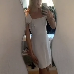 Vit klänning med puffärmar från NMPAXTON - Säljer en superfin vit klänning med puffärmar och öppen rygg från NMPAXTON. Klänningen har snörning i ryggen och en kort längd som gör den perfekt för sommarens fester. Den är både stilren och trendig, perfekt för studenten eller andra speciella tillfällen.