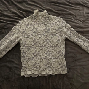 Ljusblå spetsblus från BikBok - Säljer en elegant ljusblå spetsblus från BikBok i storlek XS. Blusen har ett vackert blommönster och långa ärmar, perfekt för en stilren look. Den höga kragen ger en extra touch av sofistikation.