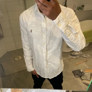 Vit skjorta från Polo Ralph Lauren - Klassisk vit skjorta från Polo Ralph Lauren i slim fit. Skjortan har långa ärmar och knappar framtill. 
