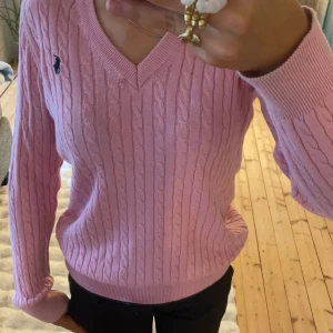 Polo Ralph Lauren tröja  - Säljer en snygg rosa kabelstickad tröja från Polo Ralph Lauren. Tröjan har en klassisk v-ringning och långa ärmar. Den ikoniska loggan är broderad på bröstet. 100% äkta🤗. Hör av dig vid frågor eller funderingar❤️priset går att diskuteras vid snabb och smidig affär😊