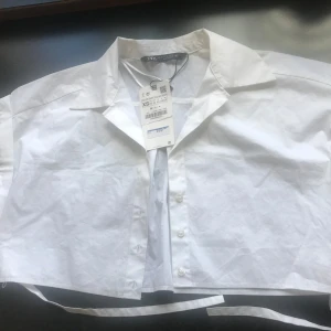 Vit croppad skjorta från Zara - Säljer en stilren vit croppad skjorta från Zara. Skjortan har knappar framtill och en klassisk krage. Perfekt för en trendig look.