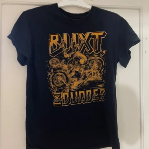 Svart t-shirt med tryck från Gildan - Cool svart t-shirt från Gildan med ett stort, gult tryck på framsidan som säger 'Blixt & Dunder'. Perfekt för en avslappnad stil. Tillverkad i bomull för en bekväm passform.