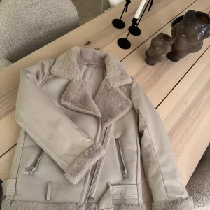 Beige jacka med foder - Har knappt använt den!!! Den är verkligen som ny. Snygg beige jacka med mjukt foder och dragkedja. Jackan har en klassisk krage och detaljer i form av bälte och dragkedjor på fickorna. Perfekt för kyligare dagar.