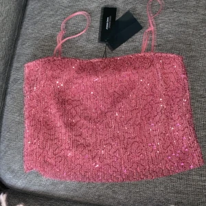 Rosa glittrig linnetopp från vero Moda - Säljer en snygg rosa glittrig linnetopp från Vero Moda. Toppen har smala axelband och är perfekt för en festlig kväll. Den är både stilren och iögonfallande med sitt glittriga material. Den är kort.