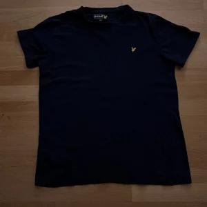 Mörkblå T-shirt från Lyle & Scott - Snygg mörkblå t-shirt från Lyle & Scott med korta ärmar och en gul broderad logga på bröstet. Perfekt för en stilren och enkel look. Passar bra till både jeans och shorts. Priset kan diskuteras 