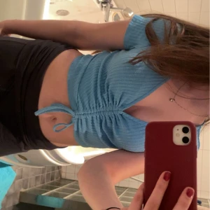 Blå ribbad topp - Säljer en snygg blå ribbad topp med korta ärmar och v-ringning. Toppen har en knytning framtill som ger en fin detalj och är croppad för en modern look.