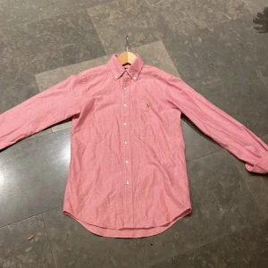  skjorta från Ralph Lauren - Säljer en klassisk rosa skjorta från Ralph Lauren i storlek XS. Skjortan har långa ärmar och knappar framtill. Perfekt för en stilren look. Perfekt till sommaren