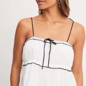 Vit topp - Söt vit topp med svarta detaljer. Luftig passform med volanger och knytband framtill. Perfekt för sommaren 🌸💄