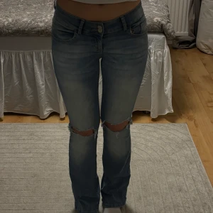 Blå jeans från Nelly - Snygga blå jeans från Nelly med hål på knäna. De har en låg midja och bootcut modell.