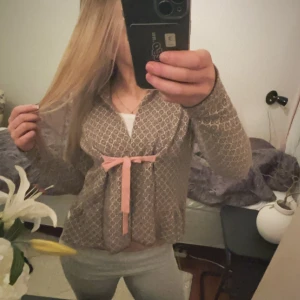 Mönstrad kofta från Odd Molly - Säljer en snygg mönstrad kofta från Odd Molly i brunt och vitt. Koftan har långa ärmar och en söt rosa rosett framtill. Perfekt för att ge din outfit en unik touch. Passar bra till både jeans och kjol!