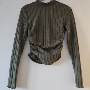 Grön ribbad tröja från Shein - Säljer en grön ribbad tröja från Shein i storlek S. Tröjan har långa ärmar och en stilren design med en hög krage. Materialet är en blandning av polyester och elastan vilket ger en skön stretch. Perfekt för en stilren look!