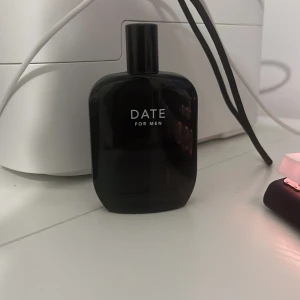Date for Men Parfym - Elegant och stilren parfymflaska i svart med texten 'Date for Men'. Perfekt för den som söker en sofistikerad doft. Flaskan har en modern design med rundade kanter och en praktisk storlek för enkel förvaring.
