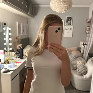 Vit kortärmad topp med detaljer - Säljer en stilren vit topp med korta ärmar och svarta randiga detaljer vid ärmsluten. Perfekt för en enkel och snygg look. Passar bra till både jeans och kjol.