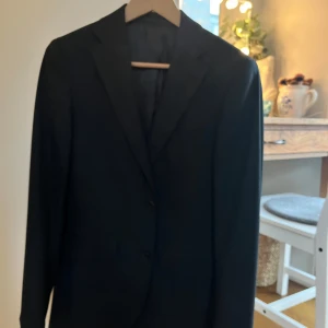 Svart kavaj-Riley - Snygg svart kavaj med två knappar framtill. Perfekt för en stilren look. Passar bra till både jeans och mer formella byxor. Perfekt för bal, student och skolavslutning med mera. Även snygg till vardagliga aktiviteter eller kalas/fest.Han på bilden är 181cm, den är lite liten för honom. Den är använd 2-5 gånger så helt oanvänd inprincip. Nypris 1799kr.