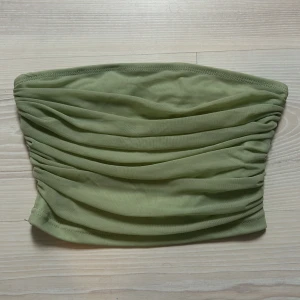 Grön tubtopp - Snygg grön tubtopp med rynkade detaljer. Perfekt för varma dagar och kan enkelt matchas med olika outfits. Toppen är elastisk och bekväm att bära.