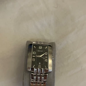 Rektangulär klocka från GANT - Elegant rektangulär klocka från GANT med en stilren svart urtavla och silverfärgade detaljer. Armbandet är i rostfritt stål med en klassisk länkdesign. Perfekt för den som söker en tidlös accessoar. Pris kan diskuteras 