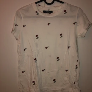 Vit t-shirt med rosor från Bershka - Säljer en söt vit t-shirt från Bershka med små röda rosor som mönster. I nytt skick, bara använd en enstaka gång.