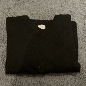 Svart kortärmad tröja från H&M - Säljer en stilren svart kortärmad tröja från H&M. Tröjan har en v-ringad hals och ribbade kanter. Perfekt för en minimalistisk look. Passar bra till både jeans och kjol. Tröjan är i storleken M, men har tvättats och blivit mindre. Nu är tröjan ungefär i storleken S!