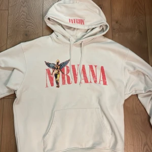 Vit Nirvana hoodie - Säljer en vit Baggy hoodie med Nirvana tryck fram och bak. Hoodien har en stor ficka framtill och justerbar huva med snören. Perfekt för fans av bandet! 