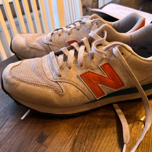 Beige sneakers från New Balance - Säljer ett par beige sneakers från New Balance med orange och turkosa detaljer. Helt ok skick 