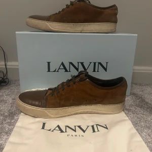Bruna sneakers från Lanvin - Snygga bruna sneakers från lanvin med snygg mocka . Skorna har en klassisk snörning och en vit sula som ger en stilren look. Perfekta för en avslappnad men ändå elegant stil. 