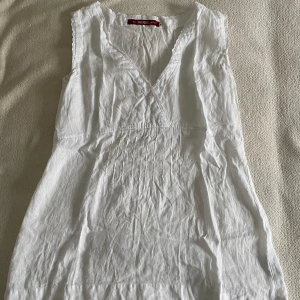 Vit ärmlös blus från Indiska - Säljer en vit ärmlös blus från Indiska med v-ringning och spetsdetaljer längs kanterna. Aldrig använd. Stryker såklart innan jag skickar.