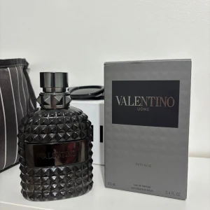 Valentino Uomo Intense Eau de Parfum - Säljer en lyxig Valentino Uomo Intense Eau de Parfum i en elegant flaska med nitar. Doften är intensiv och maskulin, perfekt för den som vill sticka ut. Flaskan rymmer 100 ml och kommer i en stilren grå förpackning. Perfekt för den som älskar exklusiva dofter. 90% kvar