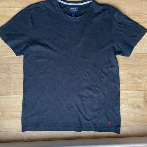 Svart t-shirt från Ralph Lauren - Säljer en klassisk svart t-shirt från Ralph Lauren med det ikoniska röda broderade logotypen på framsidan. T-shirten är kortärmad och tillverkad i mjuk bomull. Perfekt för en stilren och avslappnad look.