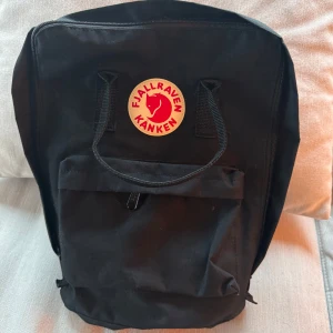 Fjällräven Kånken - Fjällräven Kånken – Nästintill oanvänd!  Säljer en nästintill oanvänd Fjällräven Kånken i svart, som bara har använts ett fåtal gånger vid photo shoots . Väskan är i nyskick, mest samlat damm.   Perfekt för både vardag och friluftsliv – lätt, slitstark och bekväm att bära.  Detaljer: -Original Fjällräven Kånken -Rymmer 16L -Klassisk design med sittunderlag i ryggfickan -Justerbara remmar  Nypris: 1299kr på Fjällrävens egna hemsida.