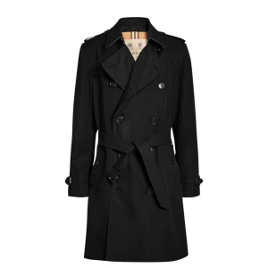Svart trenchcoat från Burberry - Säljer en klassisk svart trenchcoat från Burberry med dubbelknäppning och bälte i midjan. Jackan har långa ärmar och stilrena detaljer som axelklaffar och knappar vid ärmsluten. Perfekt för en elegant look. Kemtvättad bälte och original väskan finns med. 