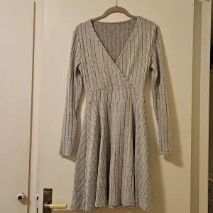 Grå ribbad klänning från Shein - Säljer en stilren grå ribbad klänning från Shein med omlott-design och v-ringning. Klänningen har långa ärmar och en skön passform som passar perfekt för kyligare dagar. Perfekt för dig som vill ha en enkel men snygg look.