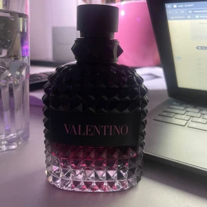 Valentino Uomo Born In Roma Intense 100ml - Snygg parfymflaska från Valentino med en lyxig design. Flaskan är dekorerad med ett mönster av små pyramider och har en gradient från mörkt till ljust glas. Perfekt för den som vill ha en elegant touch på sin doftsamling. Runt 70ml kvar